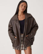 Blouson femme motard en similicuir marron avec zip asymétrique et motif de surpiqûres.