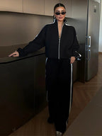 Ensemble sport femme noir, composé d'une veste zippée et d'un pantalon large en matériau léger et respirant.