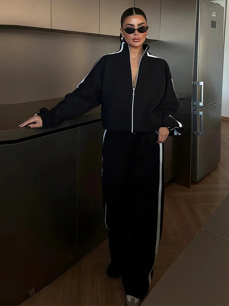 Ensemble sport femme noir, composé d'une veste zippée et d'un pantalon large en matériau léger et respirant.
