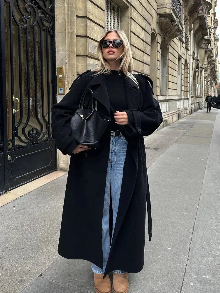 Langer schwarzer Mantel für Damen aus warmem Material, mit Taillengürtel und breiten Revers für einen eleganten Schnitt.