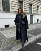 Lang schwarzer Damenmantel aus Wolle mit breiten Revers und taillierbarem Gürtel für eine feminine Silhouette.