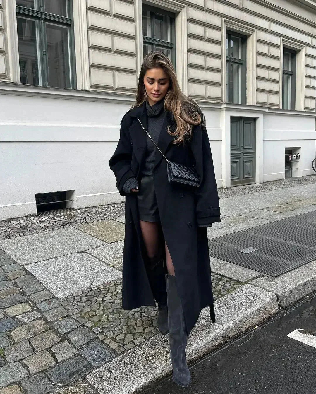 Lang schwarzer Damenmantel aus Wolle mit breiten Revers und taillierbarem Gürtel für eine feminine Silhouette.