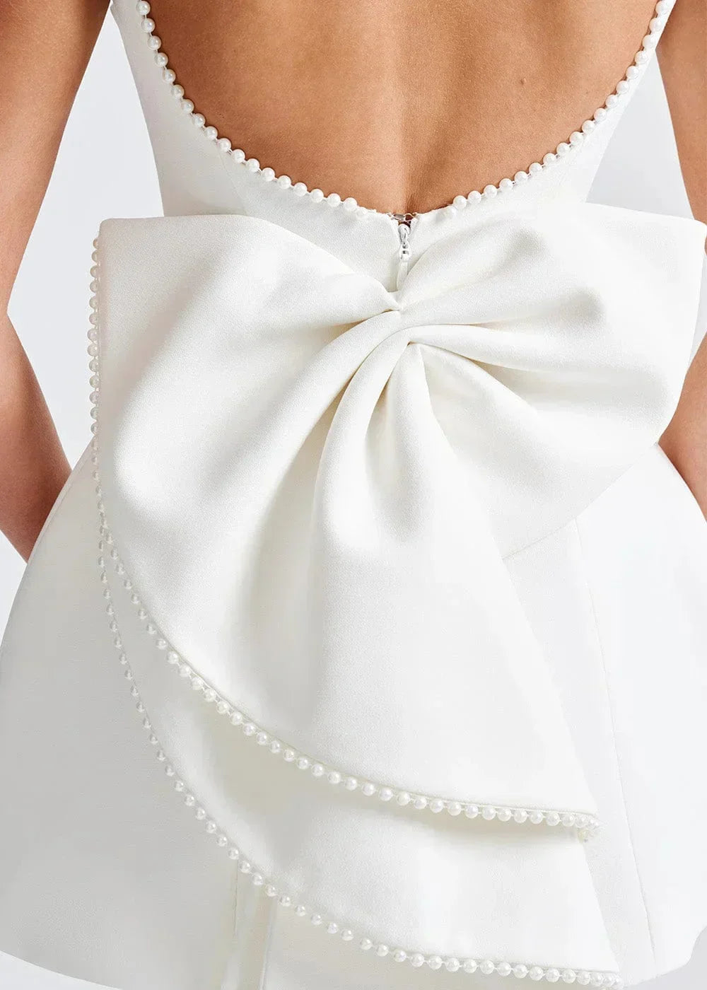 Mini robe dos nu ajustée avec grand nœud et perles, en tissu léger, parfaite pour les soirées élégantes.