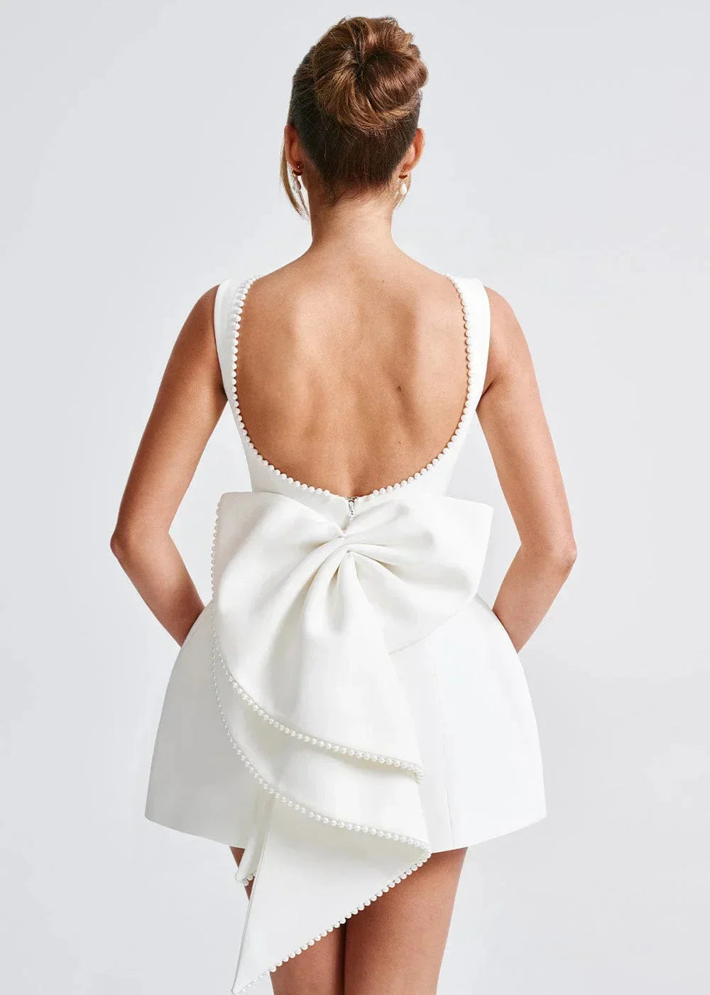 Mini robe dos nu ajustée avec grand nœud, ornée de perles, parfaite pour une soirée élégante. Fabrication douce et…