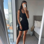 Mini robe noire en tissu léger, perlée avec découpes, manches et épaules nues, parfaite pour soirées et événements élégants.