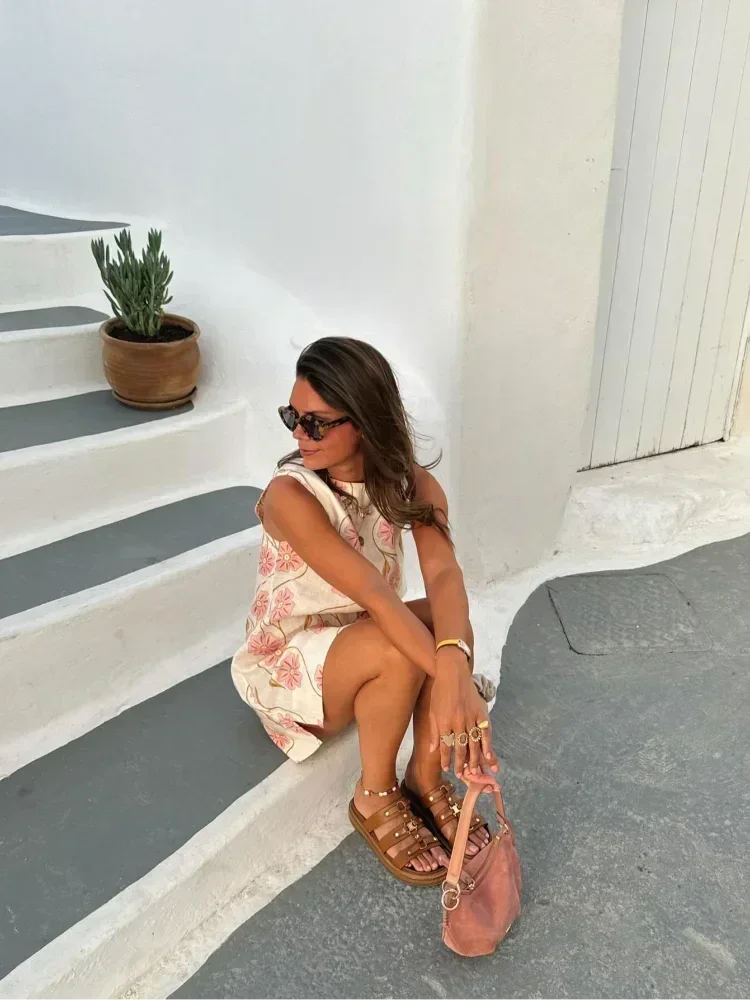 Mini robe sans manches en tissu léger blanc, ornée de fleurs roses, idéale pour les journées d'été ensoleillées.