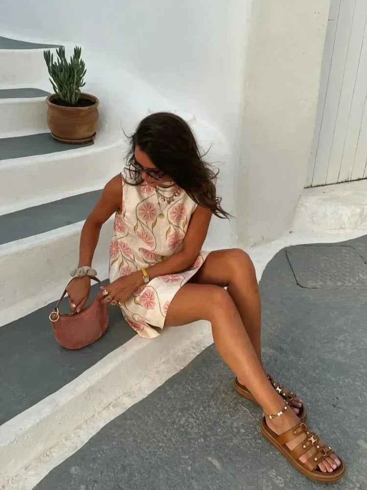 Mini robe sans manches en tissu léger blanc avec motifs de fleurs roses, idéale pour les journées d'été.