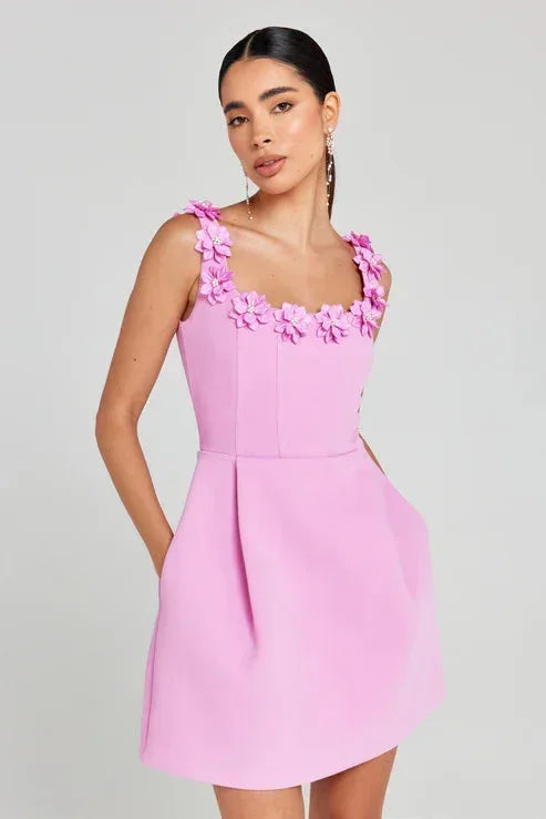 Robe courte rose en tissu léger, sans manches, avec détails floraux et encolure ajustée, idéale pour les fêtes d'été.