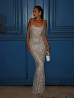 Robe longue argentée à sequins, décolleté carré, bretelles fines, en tissu scintillant pour soirées élégantes.