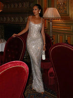 Robe longue argentée à sequins, bretelles fines, décolleté carré et tissu scintillant, idéale pour soirées élégantes.