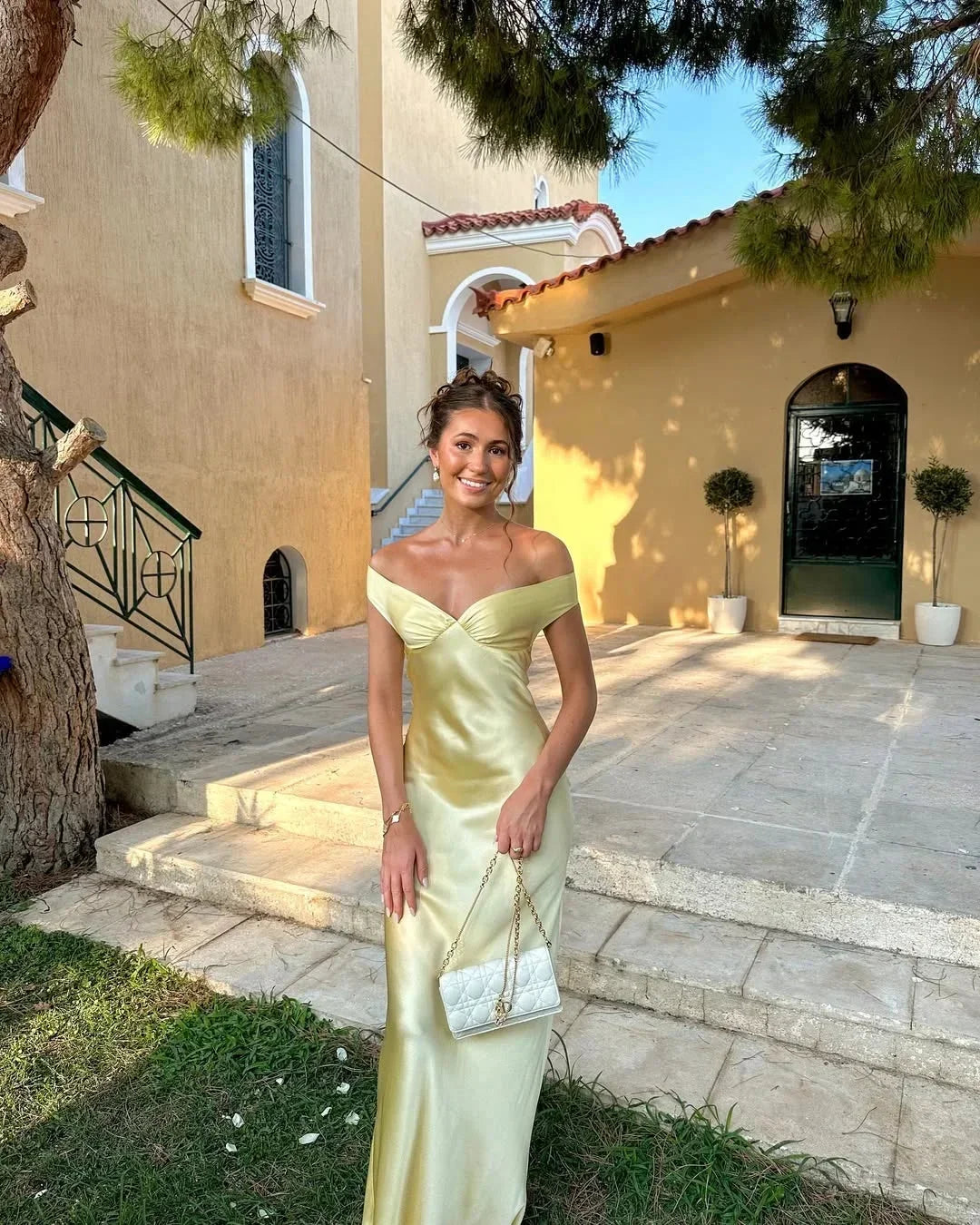 Robe longue jaune à épaules dénudées, en satin, accompagnée d'une pochette assortie pour une soirée élégante.