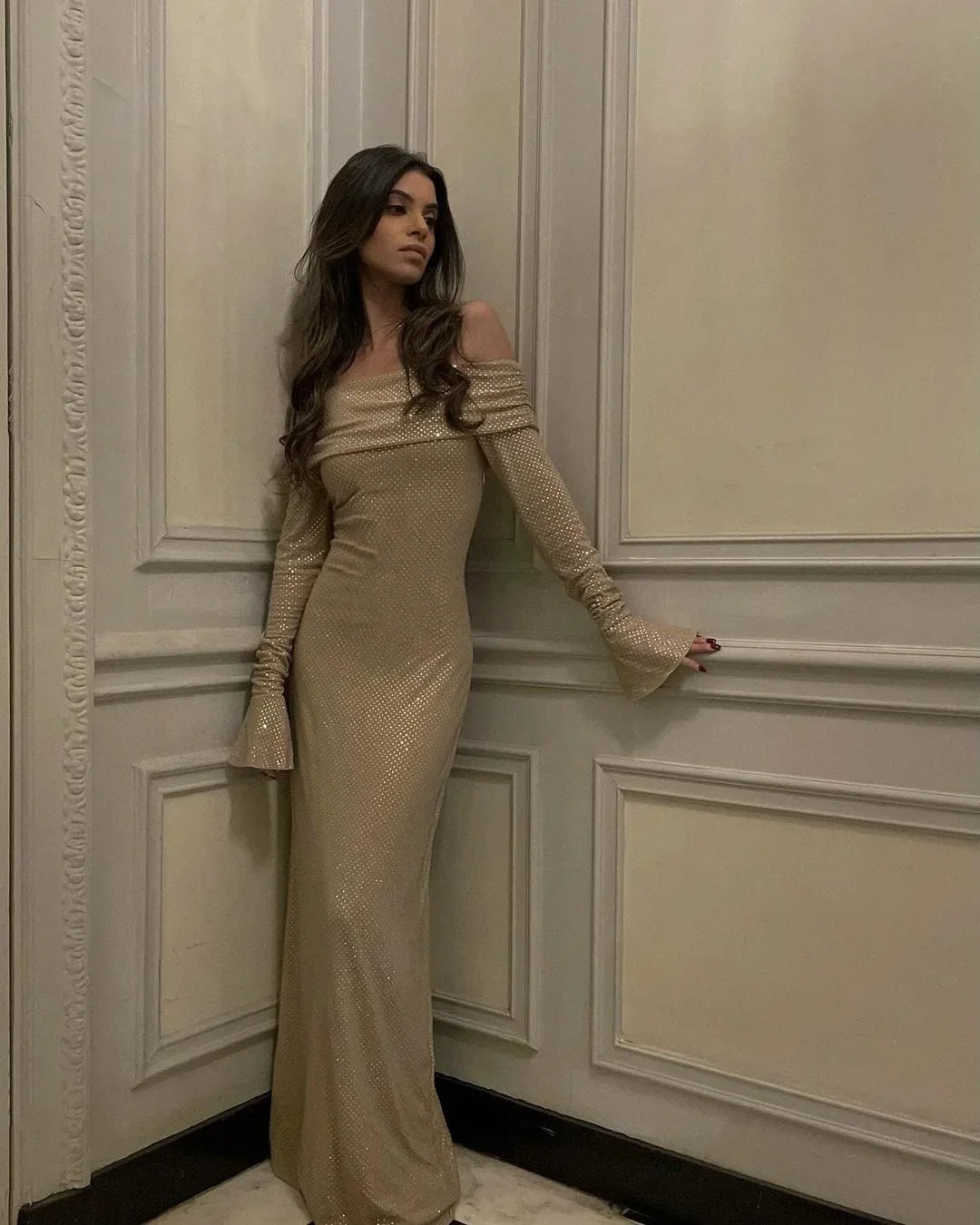 Robe longue longue en tissu brillant, épaules dénudées, manches longues, avec détails scintillants. Idéale pour les soirées.