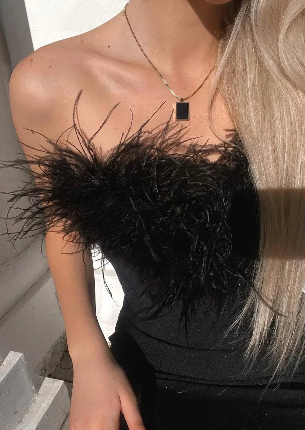 Robe longue noire sans bretelles en tissu léger, ornée d'une élégante bordure en plumes pour une soirée.