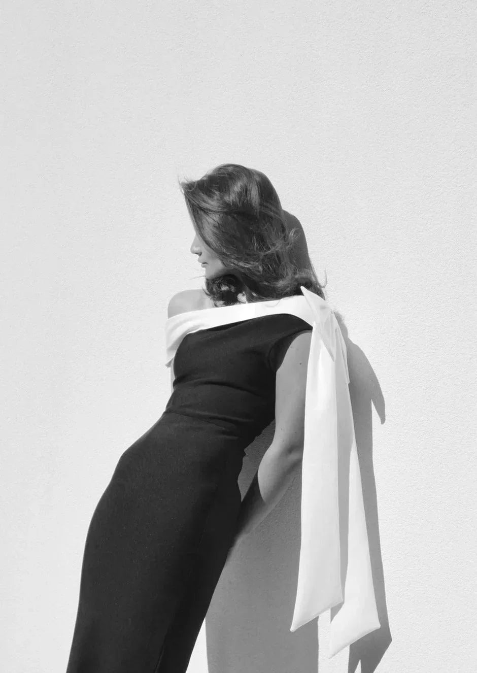 Robe midi asymétrique en tissu léger, noire et blanche, avec une épaule unique et un nœud décoratif sur le côté.