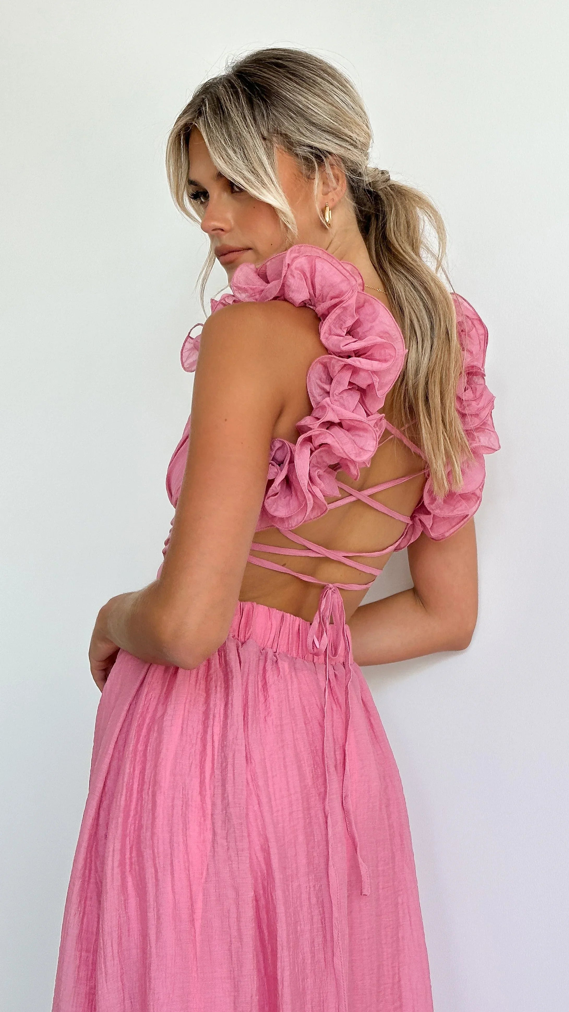 Robe midi rose en tissu léger, bustier torsadé avec volants fluides, idéale pour les occasions décontractées.