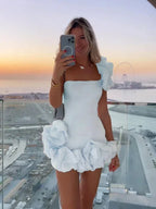 Robe courte asymétrique, épaules dénudées, volants, en tissu fluide pour une silhouette élégante lors des soirées.