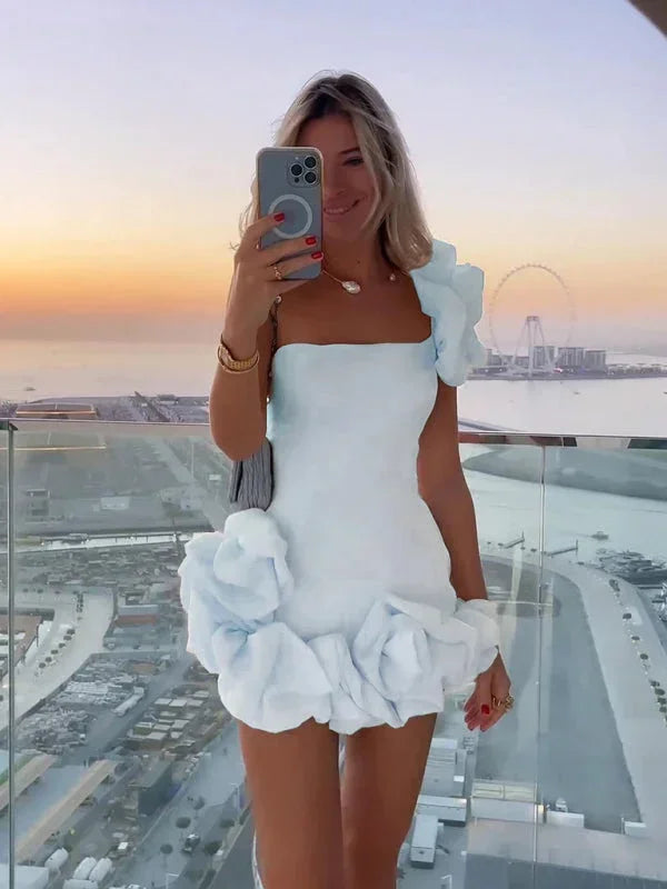 Robe courte asymétrique, épaules dénudées, volants, en tissu fluide pour une silhouette élégante lors des soirées.