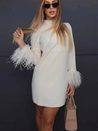 Robe courte blanche en tissu léger, manches longues ornées de plumes, coupe droite élégante idéale pour les soirées.