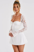 Robe courte blanche en dentelle, manches longues, dos nu, coupe ajustée idéale pour soirées cocktail. Détails délicats et…