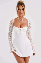 Robe courte blanche en dentelle avec manches longues et dos nu, offrant une coupe ajustée parfaite pour les cocktails élégants.