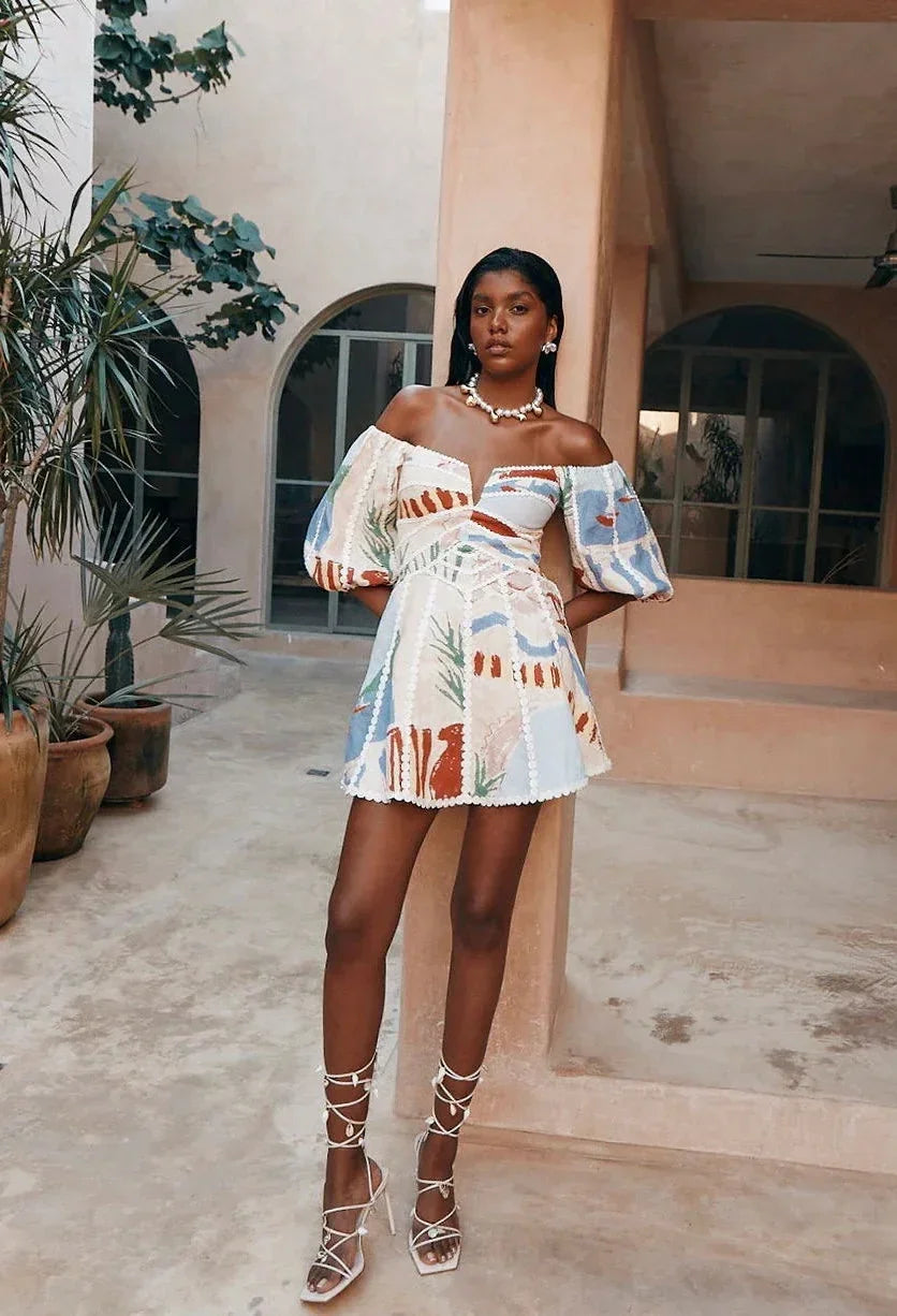 Robe courte blanche en coton léger, imprimée avec manches bouffantes et épaules dénudées, idéale pour l'été à la plage.