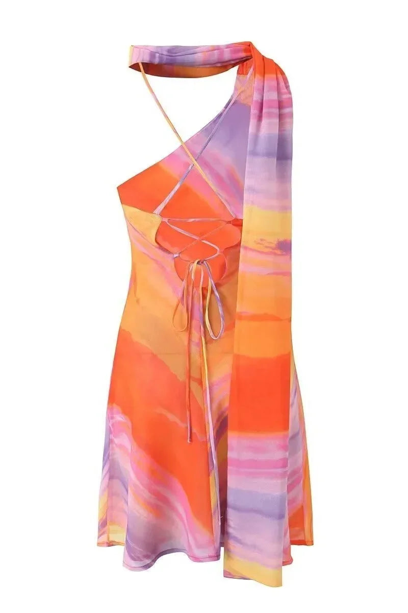 Robe courte dégradé aux couleurs de coucher de soleil, col licou et coupe asymétrique, en tissu fluide pour soirée d'été.