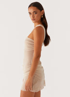 Robe courte drapée beige à une épaule, en tissu léger, avec un design asymétrique et des détails élégants pour soirée.