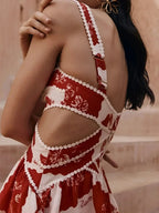 Robe courte florale rouge en coton léger, ornée de pompons blancs, idéale pour les journées d'été à la plage.