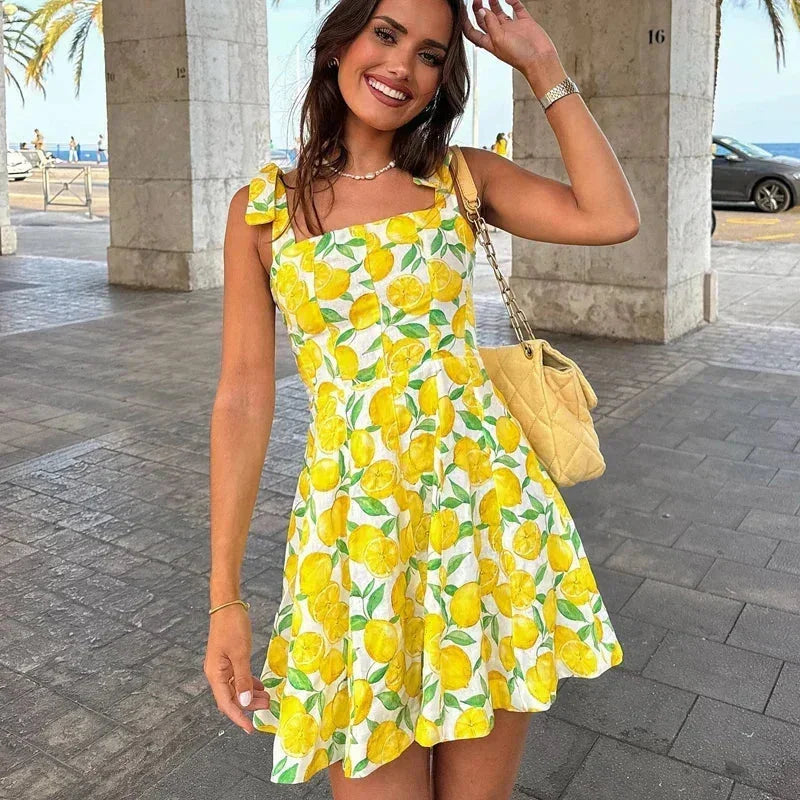Robe courte jaune à motifs citron, sans manches, en coton léger, avec encolure carrée et détail noué, parfaite pour l'été.