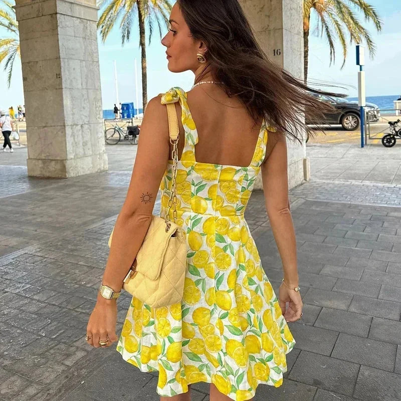Robe sans manches jaune à motifs citron, en tissu léger, avec encolure carrée et détail noué pour l'été à la plage.