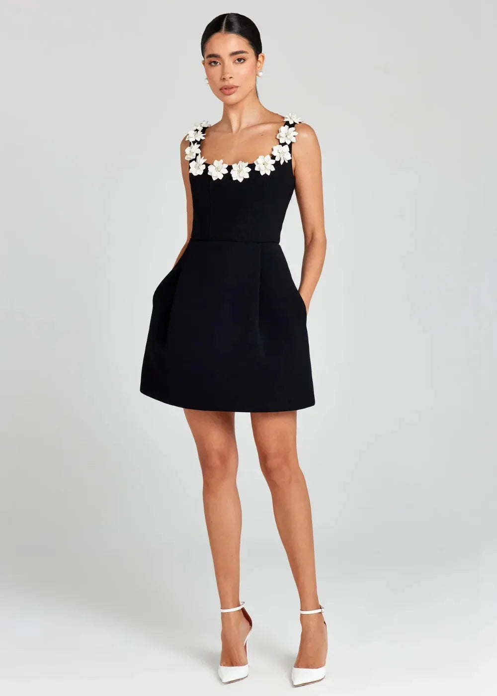 Robe courte noire sans manches avec broderies de fleurs blanches, en tissu léger, parfaite pour des soirées élégantes.