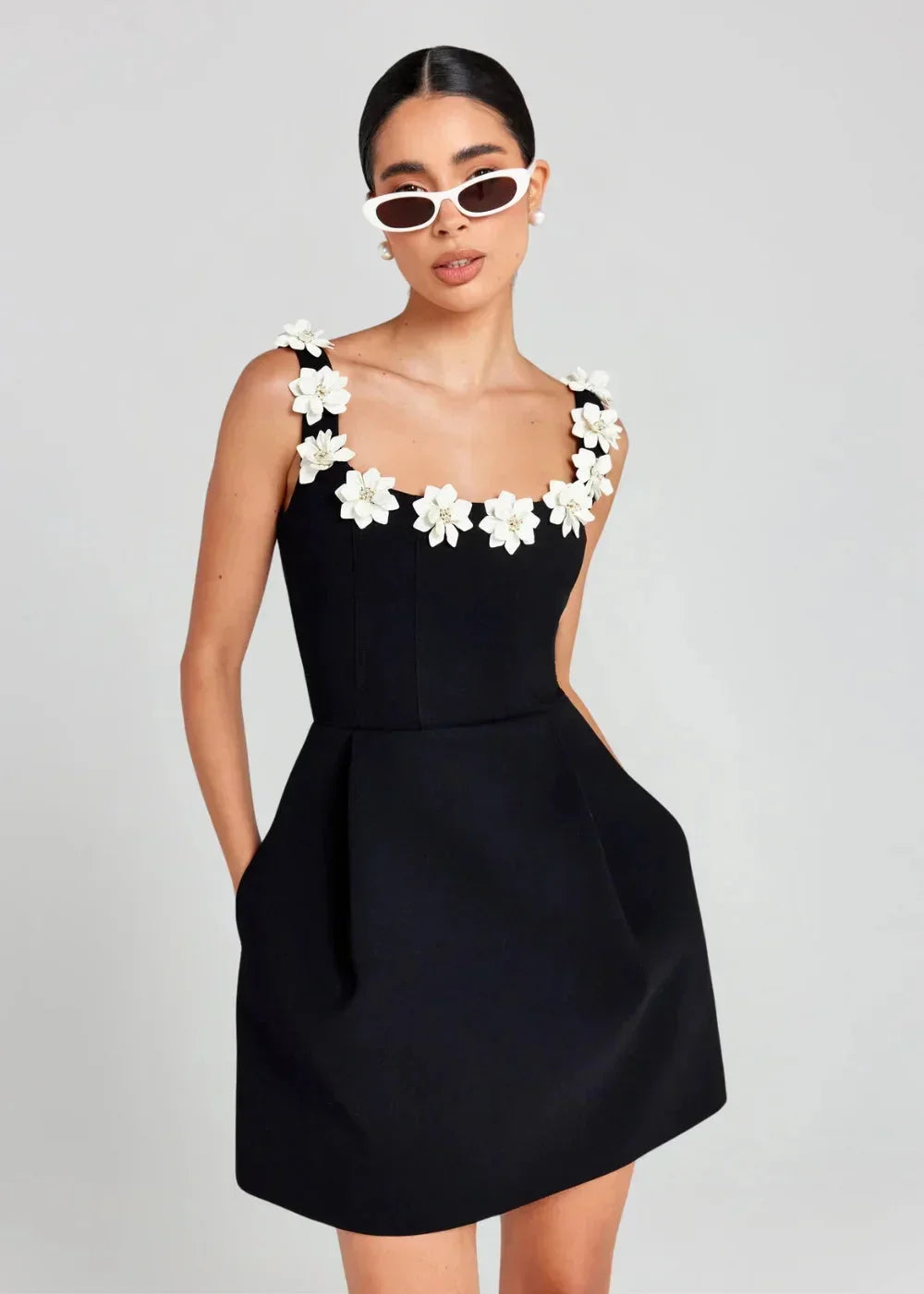 Robe courte noire sans manches, brodée de fleurs blanches, en tissu léger, parfaite pour des soirées élégantes.