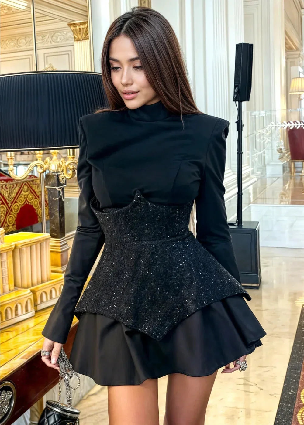 Robe courte noire à peplum, en tissu léger, ornée de sequins, avec des manches longues pour une soirée élégante.
