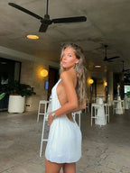 Robe courte plissée blanche sans manches, col haut, en matière légère, idéale pour des soirées estivales.