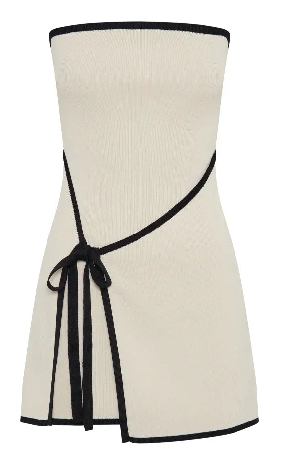 Robe courte sans manches beige, bordures noires, nœud décoratif, silhouette ajustée en tissu léger pour soirées élégantes.