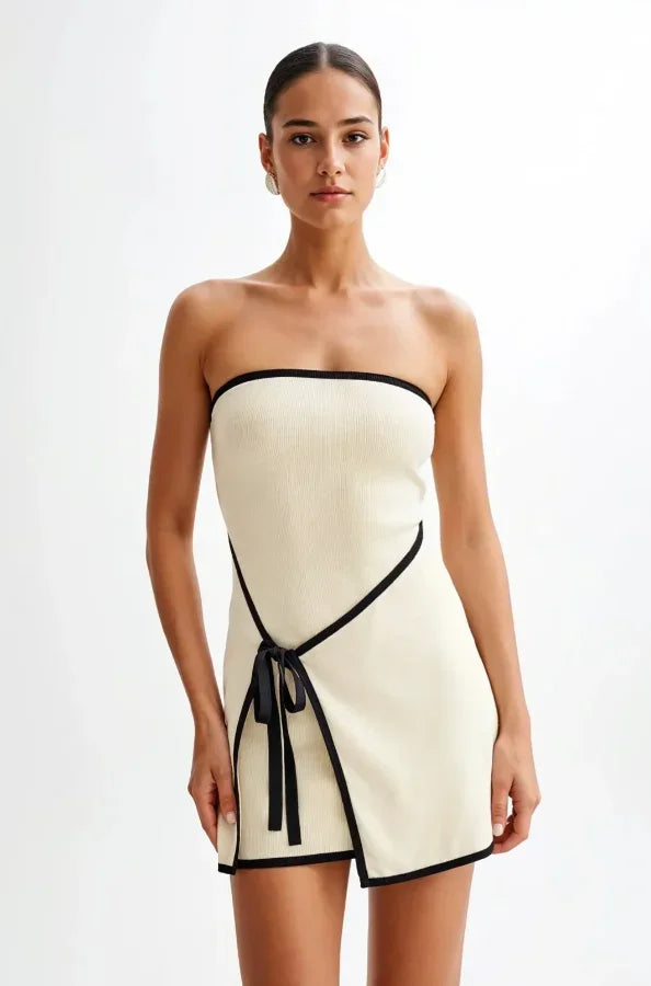 Robe courte beige sans manches avec bordures noires et nœud, coupe ajustée, idéale pour les soirées élégantes.