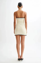 Robe courte sans manches beige avec bordures noires, nœud décoratif, en tissu léger, silhouette ajustée moderne pour soirée.