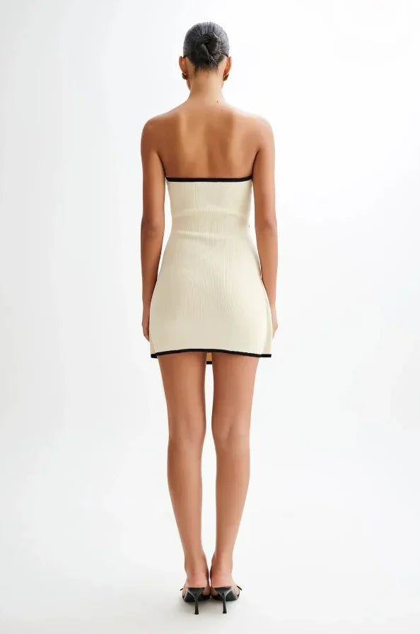 Robe courte sans manches beige avec bordures noires, nœud décoratif, en tissu léger, silhouette ajustée moderne pour soirée.