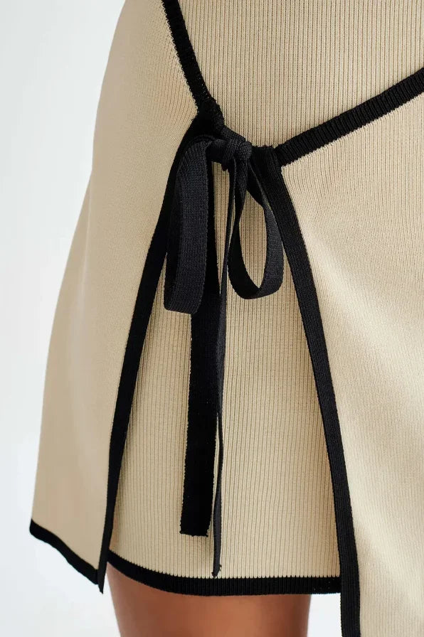 Robe courte sans manches beige avec bordures noires et nœud, silhouette ajustée, conçue en tissu léger pour soirées.