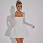 Robe courte scintillante avec manches longues transparentes, bustier carré élégant et tissu délicat pour les soirées.