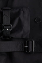 Trench-coat femme avec col montant, ceinture nouée et tissu résistant, adapté aux conditions météorologiques changeantes.