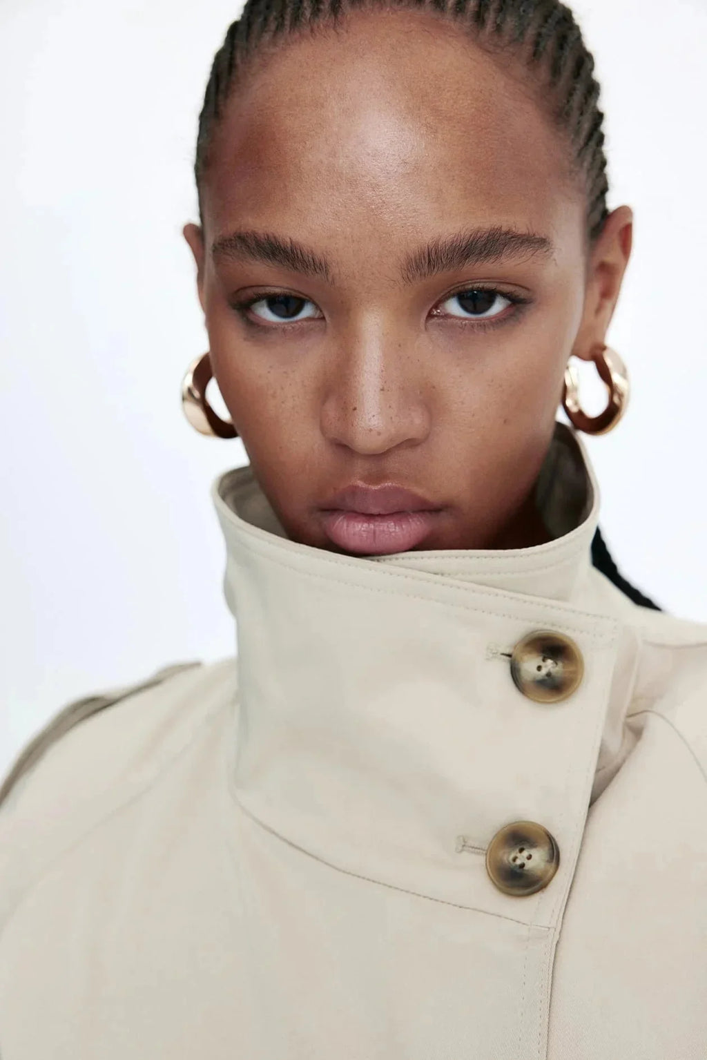 Trench-coat femme beige, col montant, coupe cintrée avec ceinture nouée à la taille.