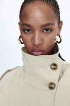 Trench-coat femme beige, col montant, coupe cintrée avec ceinture nouée à la taille.